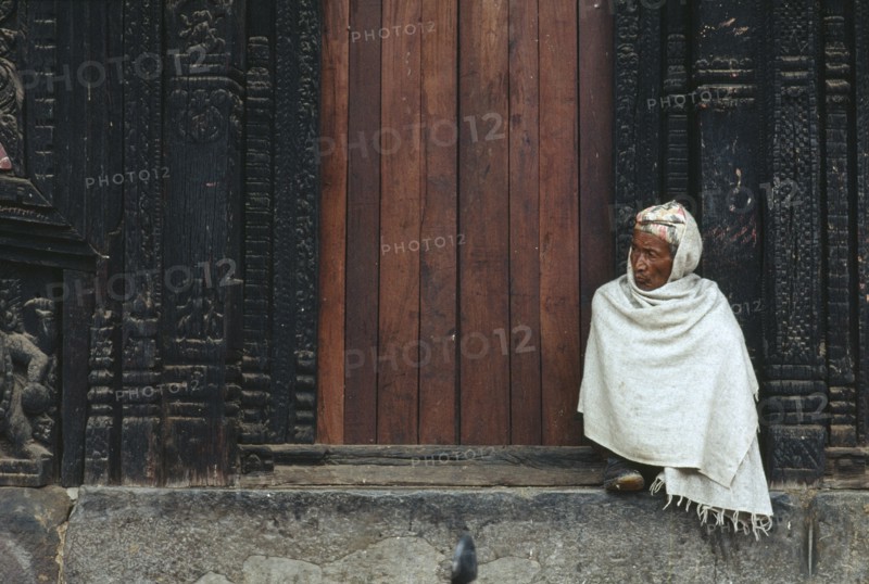 NEPAL, Bhaktapur, Man wrapped in white shawl sitting on the temple steps