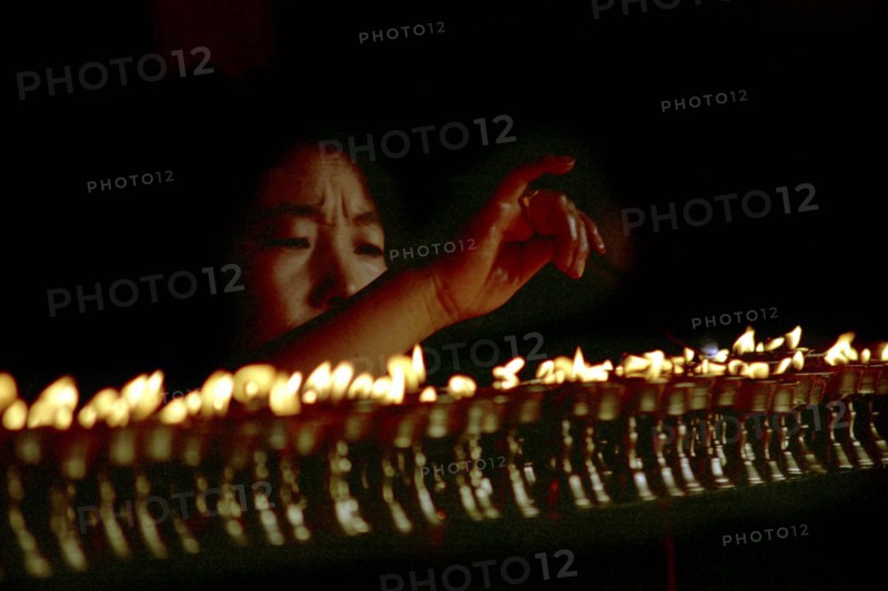 CHINA, Tibet, Lhasa, Jokhang Temple. Woman lighting prayer lamps fueled with Yak butter
