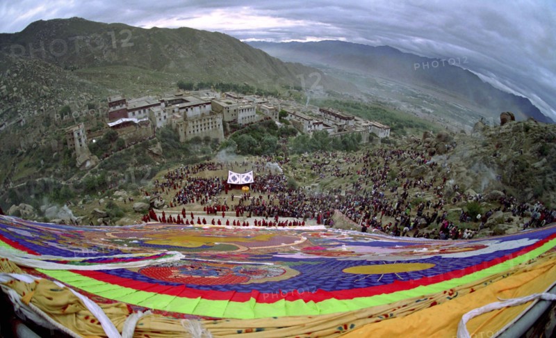 CHINA, Tibet, Drepung Monastery, Wide angled view looking down massive colourful image of buddha to Parade toward the Thangka with onlookers at a silken Thangka Buddhist ceremony for the cycle of life