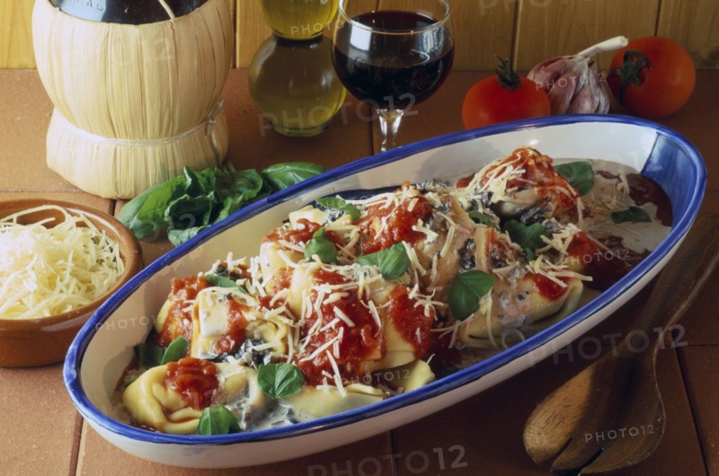 ITALY, Food and Drink, "Tortelloni in tomato and wild mushroom sauce in serving dish displayed with basil, tomatoes garlic and red wine"
