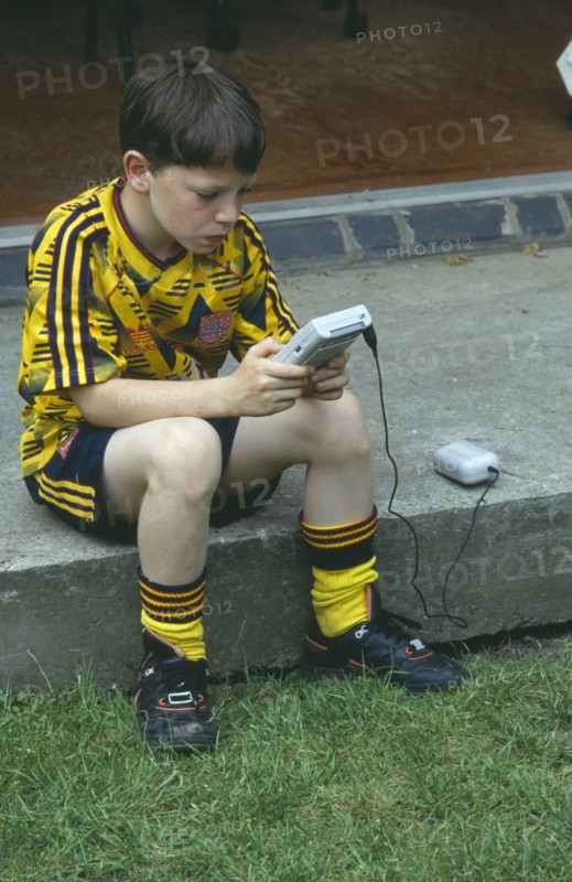 CHILDREN, Play, Computer Games, Young boy in a football kit playing a Nintendo Gameboy