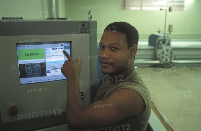 SOUTH AFRICA, Western Cape, Cape Town, Worker setting up automatic fabric cutting machine at Pre Les bedroom textiles factory