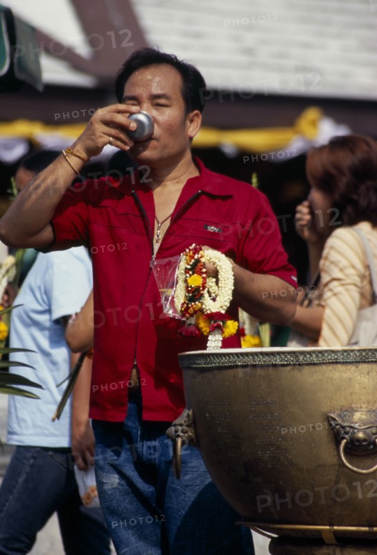 THAILAND, South, Bangkok, Wat Meuang the City pillar the most important animist shrine in Bangkok with male devotee drinking votive water