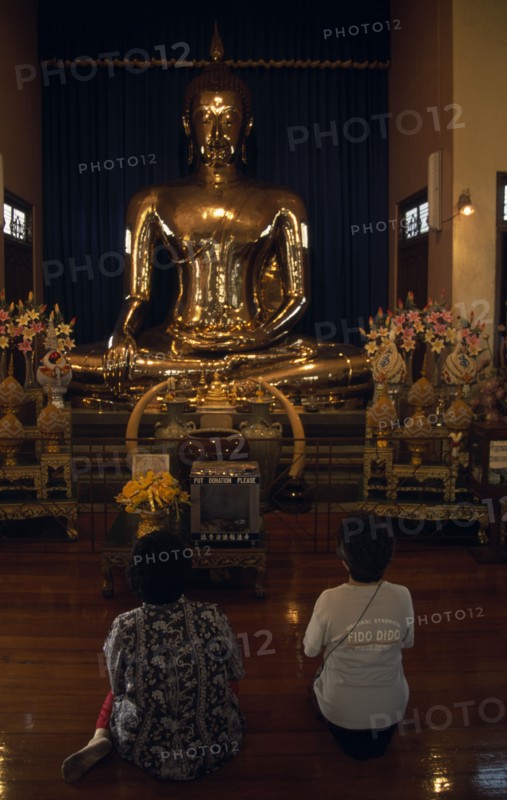 THAILAND, South, Bangkok, Wat Traimit Temple of The Golden Buddha with two women kneeling at prayer in front of the Buddha
