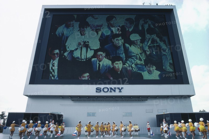 JAPAN, Tokyo, Exhibition of Technology with view of Sony Jumbotron massive Television screen and girls marching with pom poms in foreground.