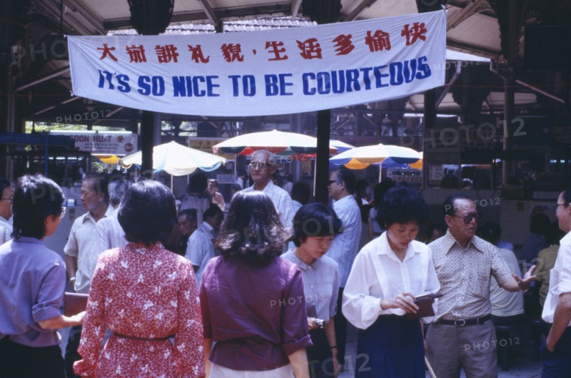 SINGAPORE, General, Street scene with mixed crowd below government banner stating Its So Nice To Be Courteous.