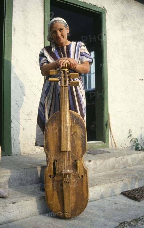 ROMANIA, Transylvania, Gimes Village, "Elderly woman with a gardon, a traditional cello like instrument played by hitting the strings with a small stick."