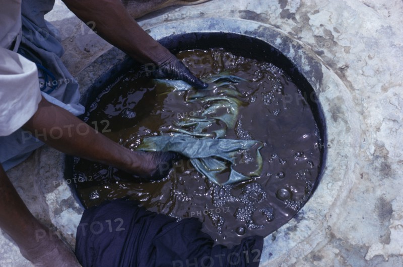 NIGERIA, Kano, Cropped view of worker and indigo dye pit.  To achieve a  dark colour requires repeated immersions.