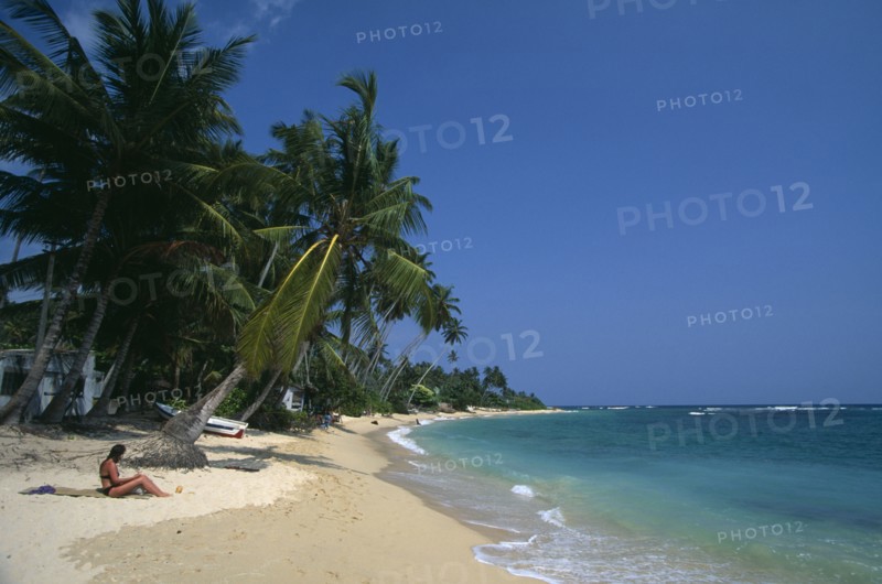 SRI LANKA, Unawatuna, Tourists on narrow strip of sandy beach fringed with palms at popular south coast resort of Unawatuna.
