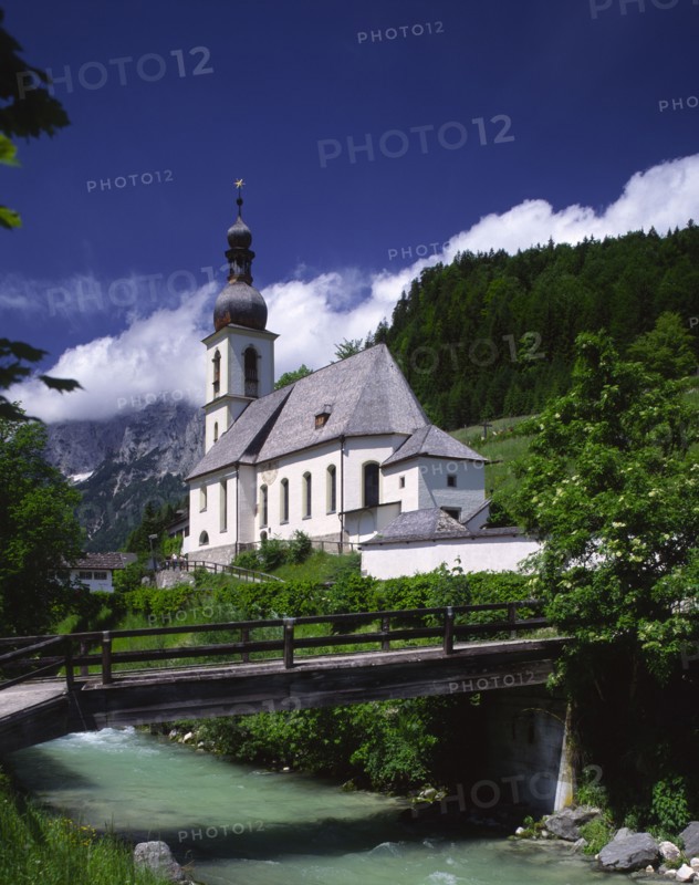 GERMANY, Bavaria, Ramsau, View over river and wooden bridge towards Ramsau Church and wooded hillside beyond.
