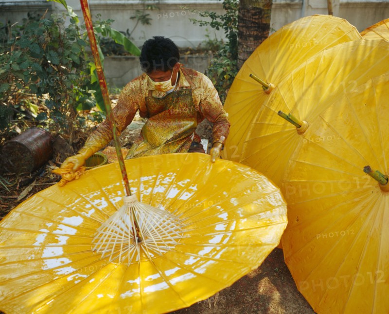 THAILAND, Chiang Mai Province, Bo Sang Village, Man spinning cotton umbrella as he applies colour finnish