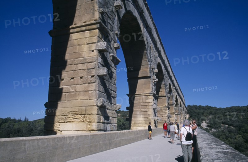 FRANCE, Languedoc Roussillon , Gard, Pont du Gard Roman aqueduct.  Tourists on bridge beside arches of water channel above.