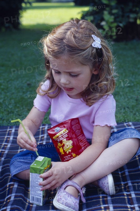 ENGLAND, West Sussex, Chichester, The Bishops Palace Gardens.  Girl aged three putting straw into carton of low sugar blackcurrant juice drink during picnic lunch.