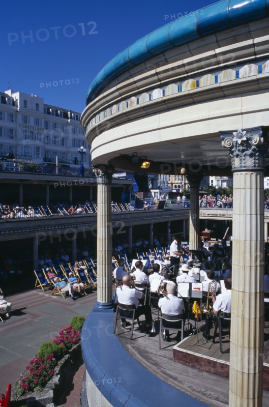 20059184 ENGLAND East Sussex Eastbourne View over the Promenade Band Stand with a brass band performing on a sunny day with spectators watching from deckchairs