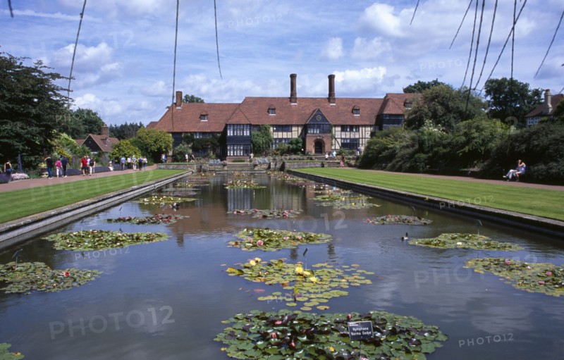 20059213 ENGLAND Surrey Woking Wisley Royal Horticultural Society Garden. View across formal pond with water lilies towards the Tudor style half timbered main entrance building.