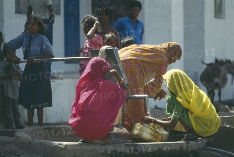 INDIA, Rajasthan, Sisarma, Women and children collecting water from village well and hand pump.