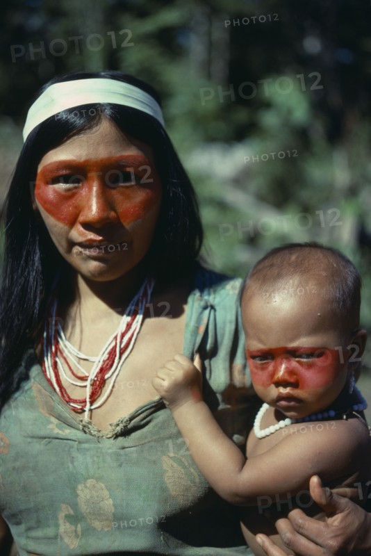 ECUADOR, Amazon, Auca Indian woman holding baby both decorated with red face paint from the achole plant.