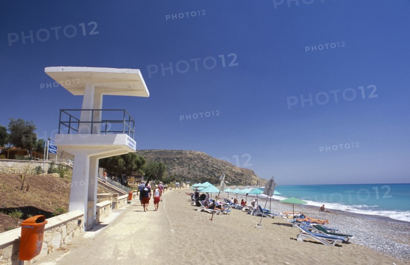CYPRUS, Pissouri Bay, Sunbathers on narrow sand and pebble beach with people walking along promenade at side and life guards tower or look out point in the foreground.