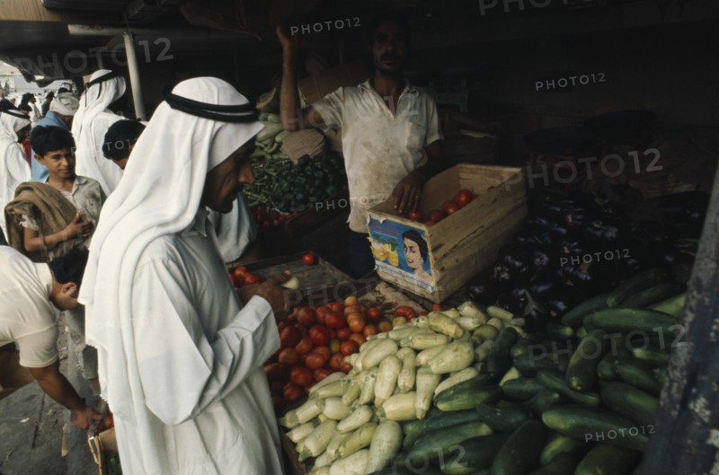 QATAR, Doha, "Man at vegetable stall in souk selling courgettes, aubergines, squash and tomatoes."