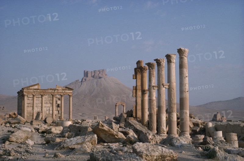SYRIA, Palmyra, Roman ruins with columns and pillars and The Islamic Fort in the distance.