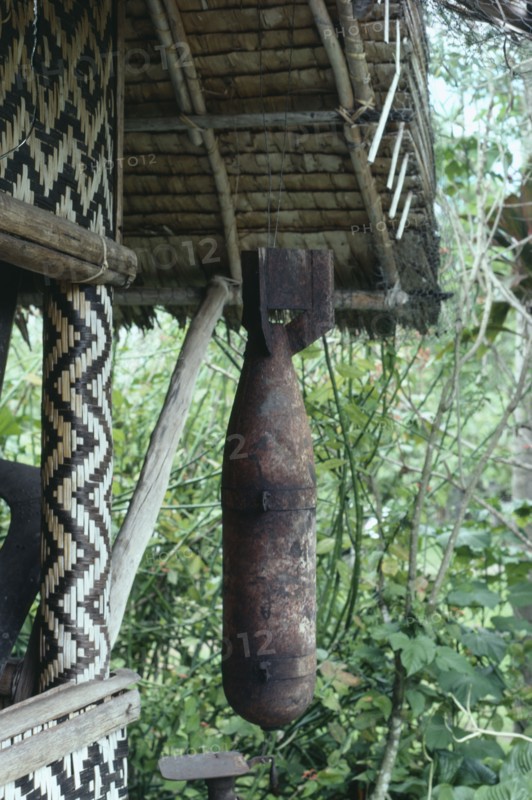 MELANESIA, Soloman Islands, Cargo cult bomb found and been venerated and hanging outside a wooden house.