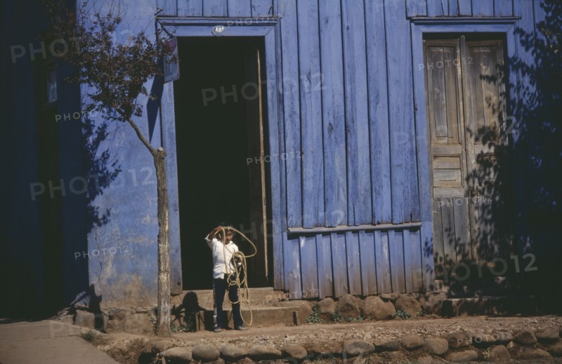 CHILE, Urban Scene, Young child standing in doorway of blue painted building swinging lasso.