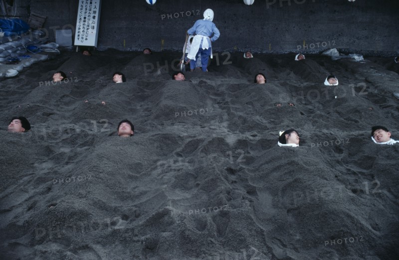 JAPAN, Kyushu, Ibusuki, Hot Sand Bath. People submerged in sand with their heads pocking out above the surface.