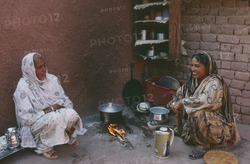 PAKISTAN, Food, Two women cooking over open wood fire in corner of building.