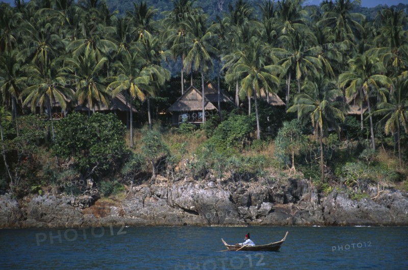 THAILAND, Krabi, Koh Lanta Yai, The Narima Spa Resort chalets amongst coconut palm trees with a man on a small fishing boat offshore