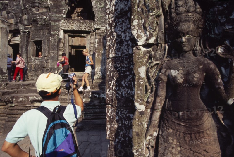 CAMBODIA, Siem Reap Province, Angkor Thom, The Bayon.  Tourists with cameras and videos with bas relief carving of apsara in the foreground.