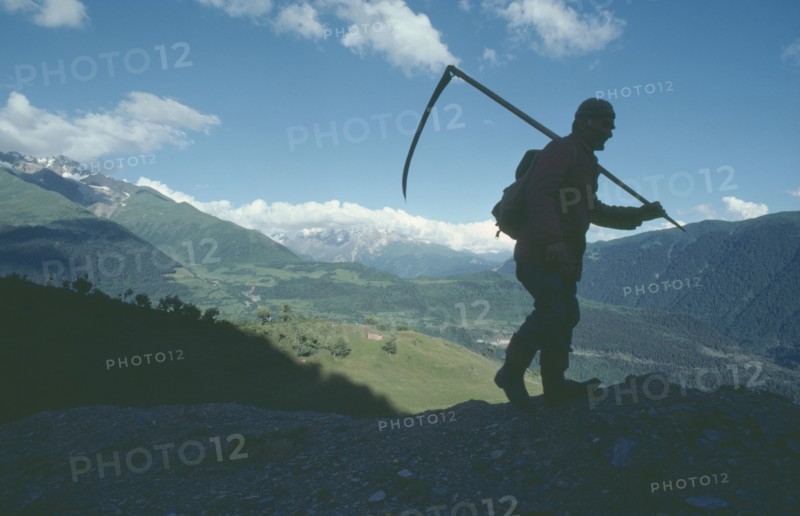 GEORGIA, Caucasus Mountains, Silhouetted figure of man carrying scythe with mountain backdrop.