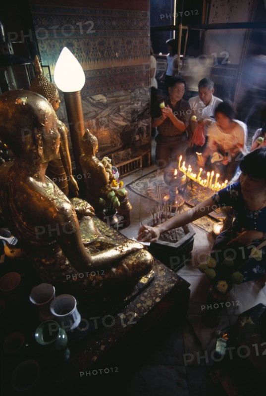THAILAND, South, Bangkok, Wat Pho small shrine beside the reclining Buddha with devotees making offerings to small Golden Buddhas
