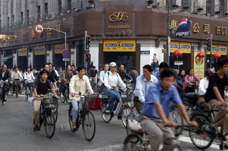 CHINA, Shanghai, Mass of cyclists passing a crossroads at the traffic lights outside the Hui Luo Co. Ltd building
