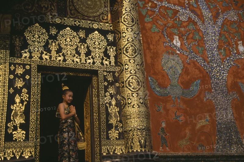 LAOS, Louangphrabang , Young girl dressed for Lao New Year at Wat Xieng Thong with highly decorated exterior.