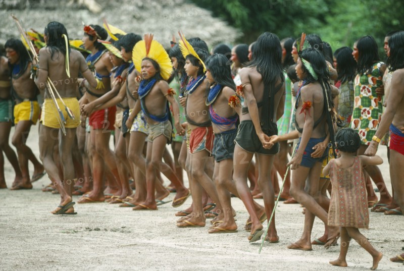 BRAZIL, Amazonas, People, Group of Xikrin Indians wearing feather head dresses and bead jewellery and with their feet and faces painted with red urucu juice.