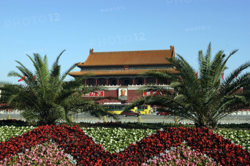 CHINA, Beijing, Tiananmen Square, Gate of Heavenly Peace or Tiananmen. View over flowerbeds and palms toward the gate building facade with large portrait of Mao
