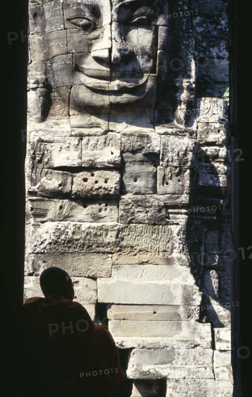 CAMBODIA, Siem Reap, Angkor Thom, Bayon Temple with a monk sitting in a doorway in front of one of the four faced towers