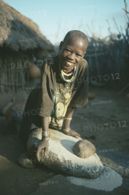 UGANDA, Karamoja, Tribal Poeple, Dodoth Karamojong girl grinding millet on stone.