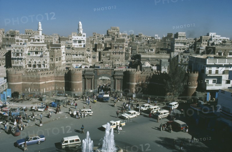 YEMEN, Sanaa, Aerial view overlooking the Old City with the city walls and entrance in the foreground with passing cars and pedestrians below
