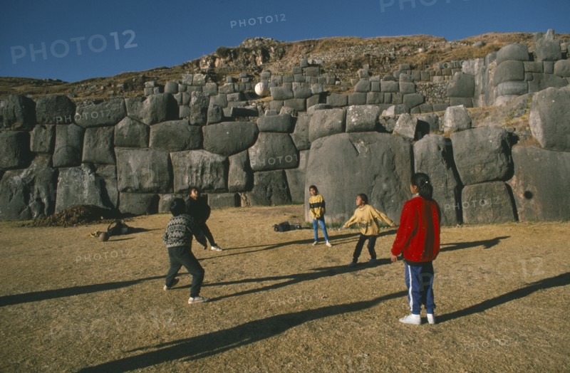 PERU, Cusco, Sacsayhuaman, Local children playing volleyball in front of walls of Inca fort on Sunday.