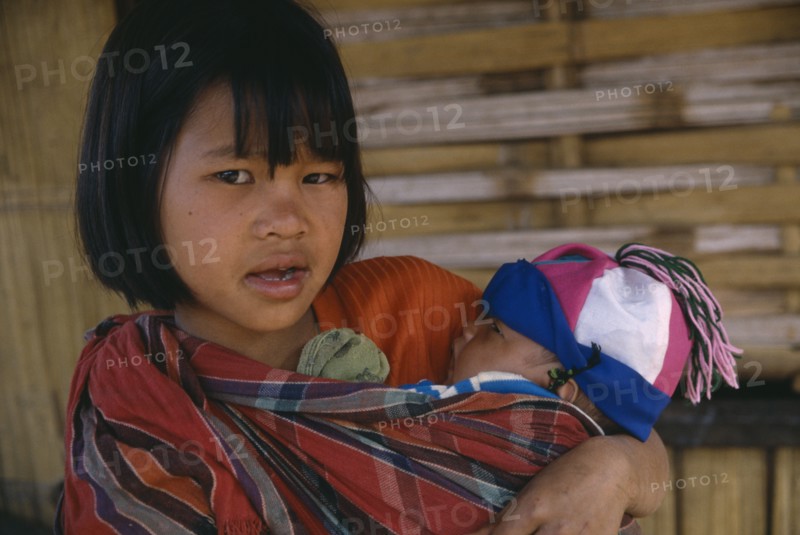 THAILAND, North, Chiang Rai , Lahu girl carrying baby in sling across her front.