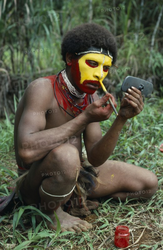 PAPUA NEW GUINEA, Southern Highlands, Tari Valley, Huli tribesman painting his face using old car wing mirror to see his reflection.