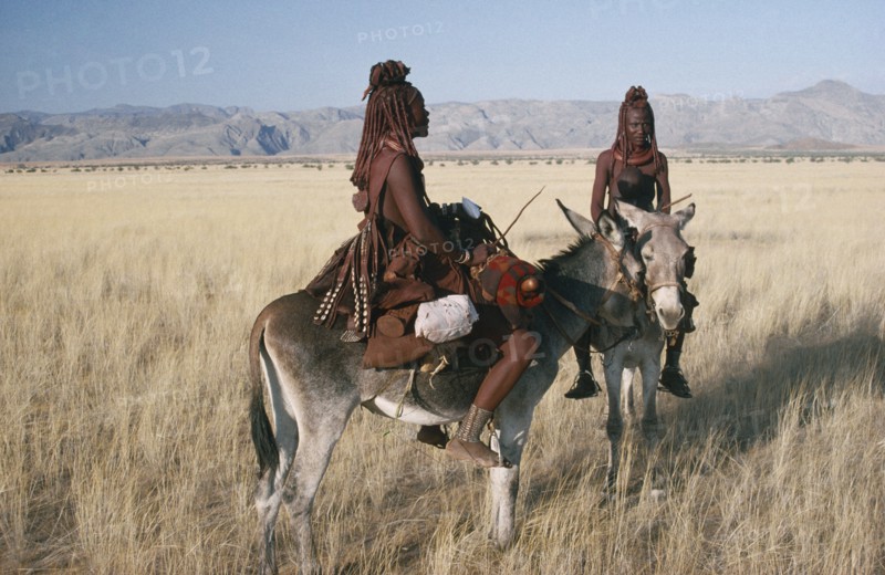 NAMIBIA, Marienfluss, Himba women and child on donkeys in grassland area.