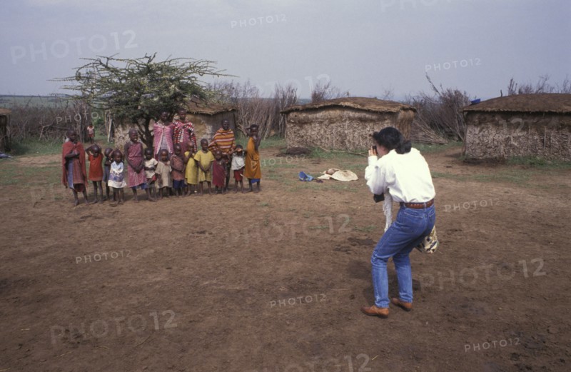 KENYA, , A Japanese tourist photographs a maasai family in a cultural manyatta set up to interface the maasai directly with tourists.