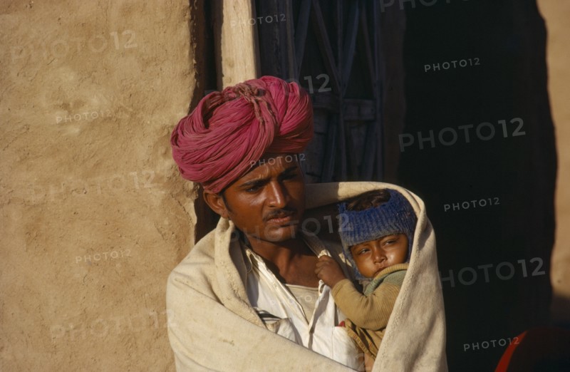 INDIA, Rajasthan, People, Man holding child wrapped in shawl on cold morning.