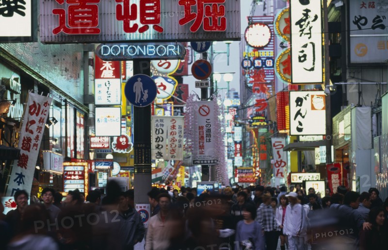 JAPAN, Honshu, Osaka, Dotonbori sign illuminated at dusk among mass of other neon signs with crowds of shoppers below