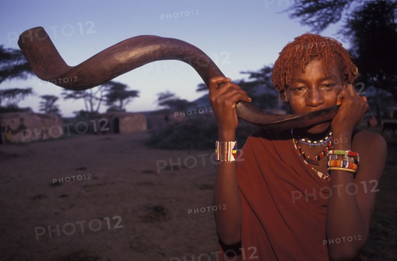 KENYA, Kajiado, A Maasai Moran blows an Ikudu horn as part of innitiation ceremony bringing the young Maasai Moran into their manhood. On blowing this horn many of the Moran go into trance.