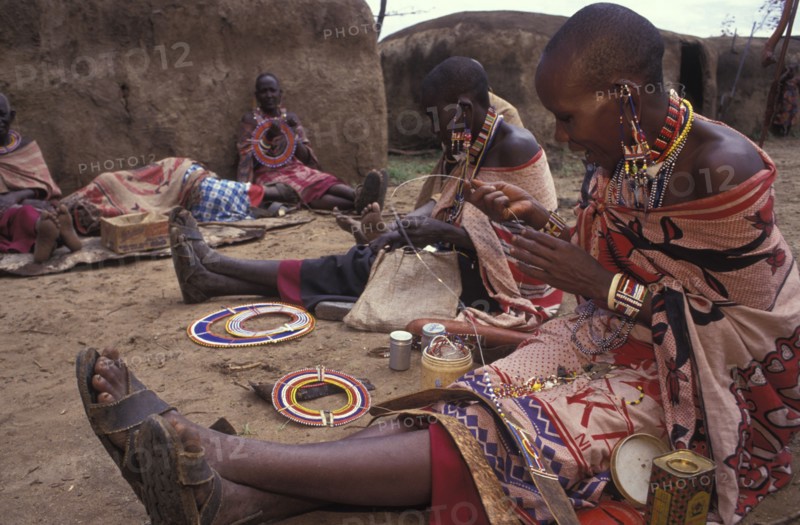 KENYA, , Maasai women making traditional crafts in a cultural  manyatta set up for tourists on the edge of the Maasai Mara game park.