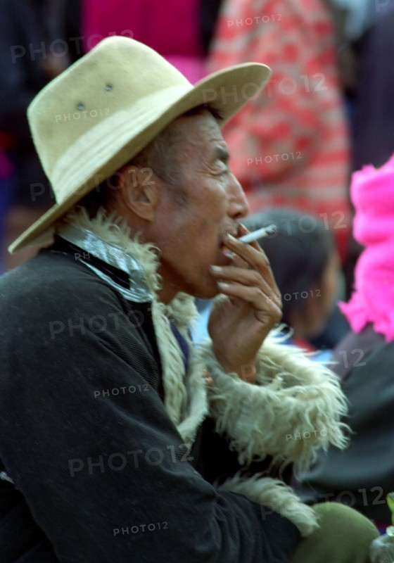 CHINA, Yunnan, Zongdian, Man in a hat and fur rimmed coat smoking a cigarette