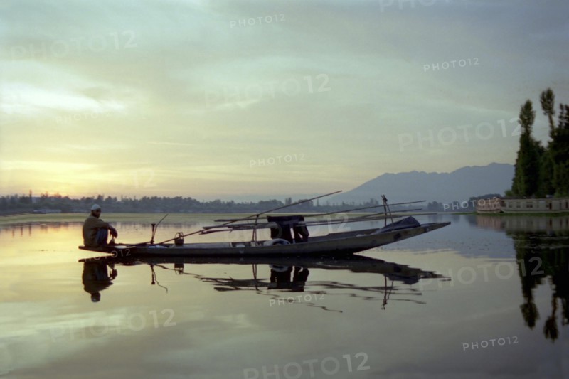 INDIA, Kashmir, Srinagar, Nagin Lake. Fisherman sitting at the very end of his canoe in the evening light